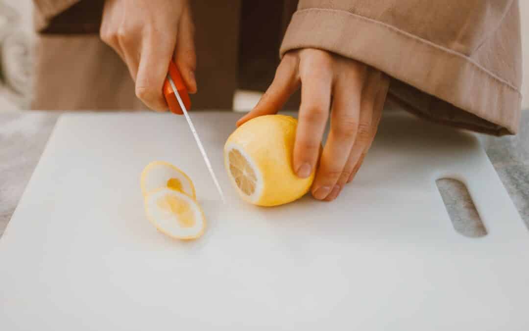image of someone cutting a lemon on a white plastic cutting board.